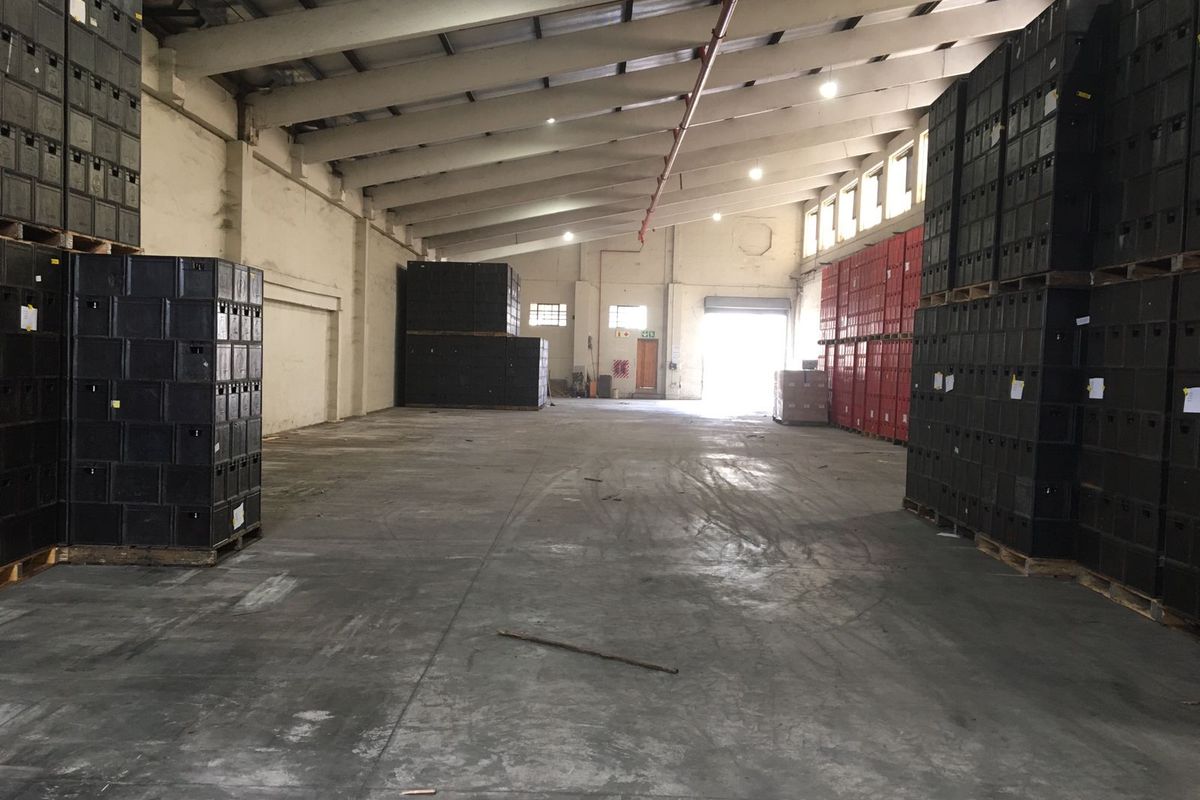 Spacious industrial warehouse featuring high ceilings with exposed trusses, concrete flooring, fire sprinkler system, and large roller shutter access.
