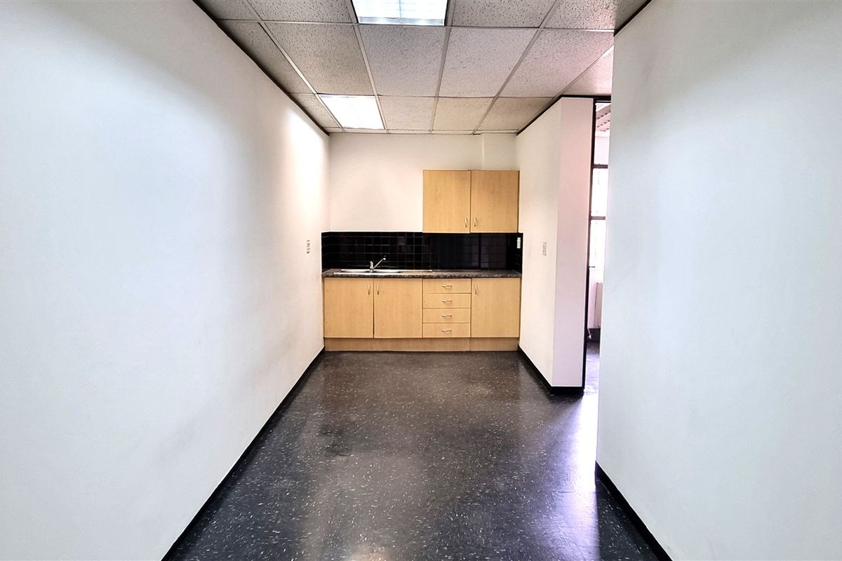 A functional office kitchenette featuring laminate cabinetry, a stainless steel sink, tiled backsplash, and suspended ceiling tiles in a clean, open layout.