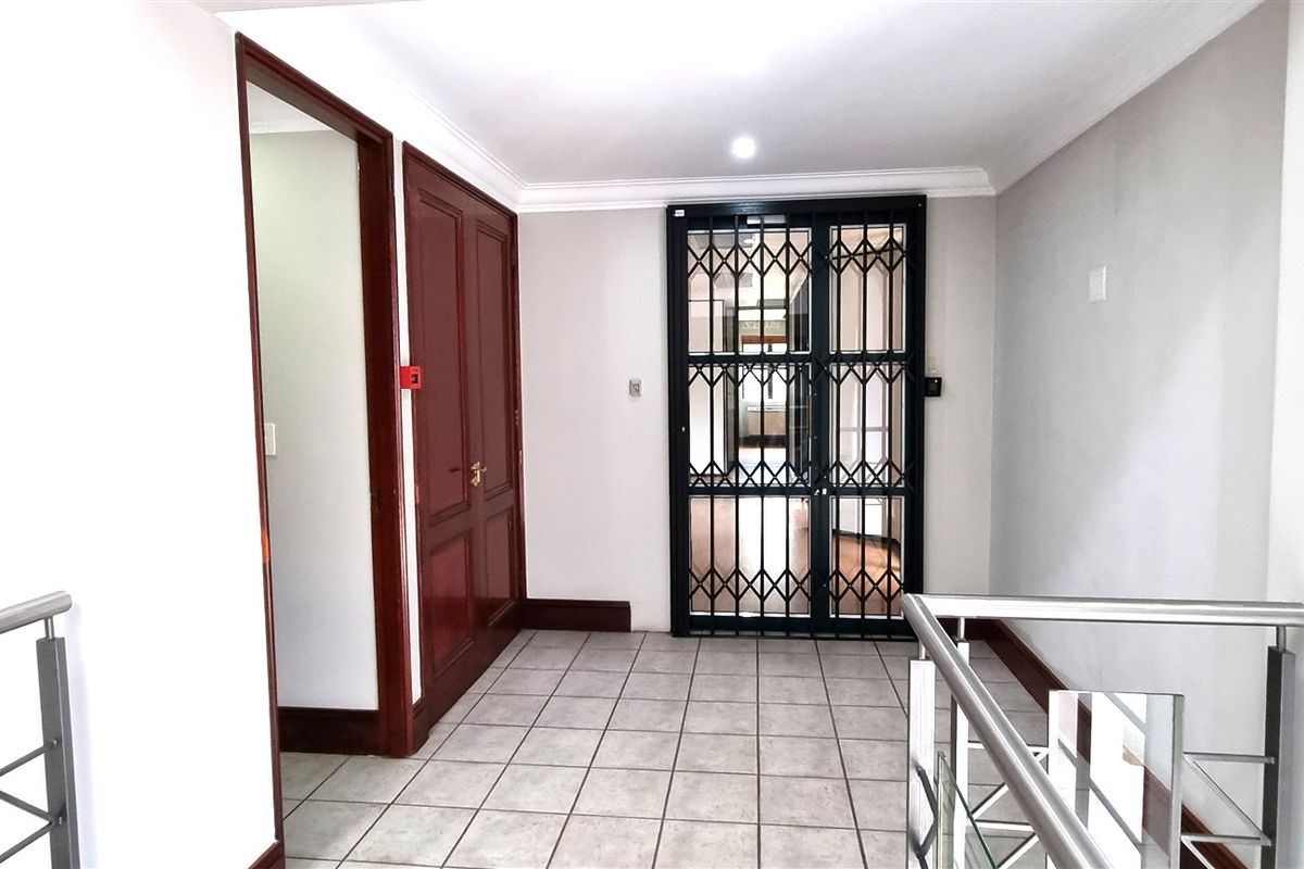 A bright and well-maintained office hallway featuring tiled flooring, a secure metal gate, and modern stainless steel balustrades.