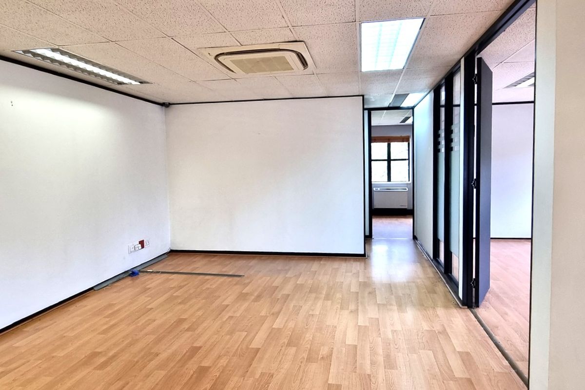 An empty, open-plan office space featuring laminate flooring, a suspended ceiling with recessed lighting, and a built-in cassette air conditioning unit.