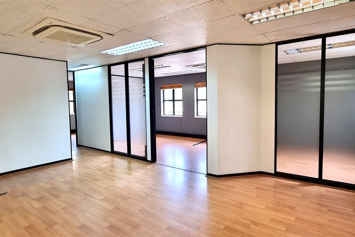 Open-plan office space featuring laminate flooring, suspended ceilings with recessed lighting, and modern glass partition walls creating separate work areas.