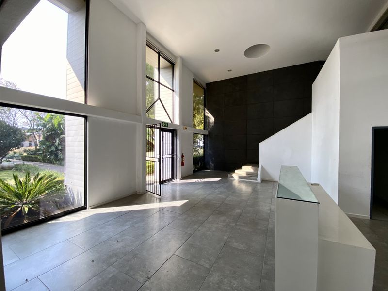 Spacious double-volume office entrance lobby featuring large windows, tiled flooring, and a built-in reception desk with modern architectural design.