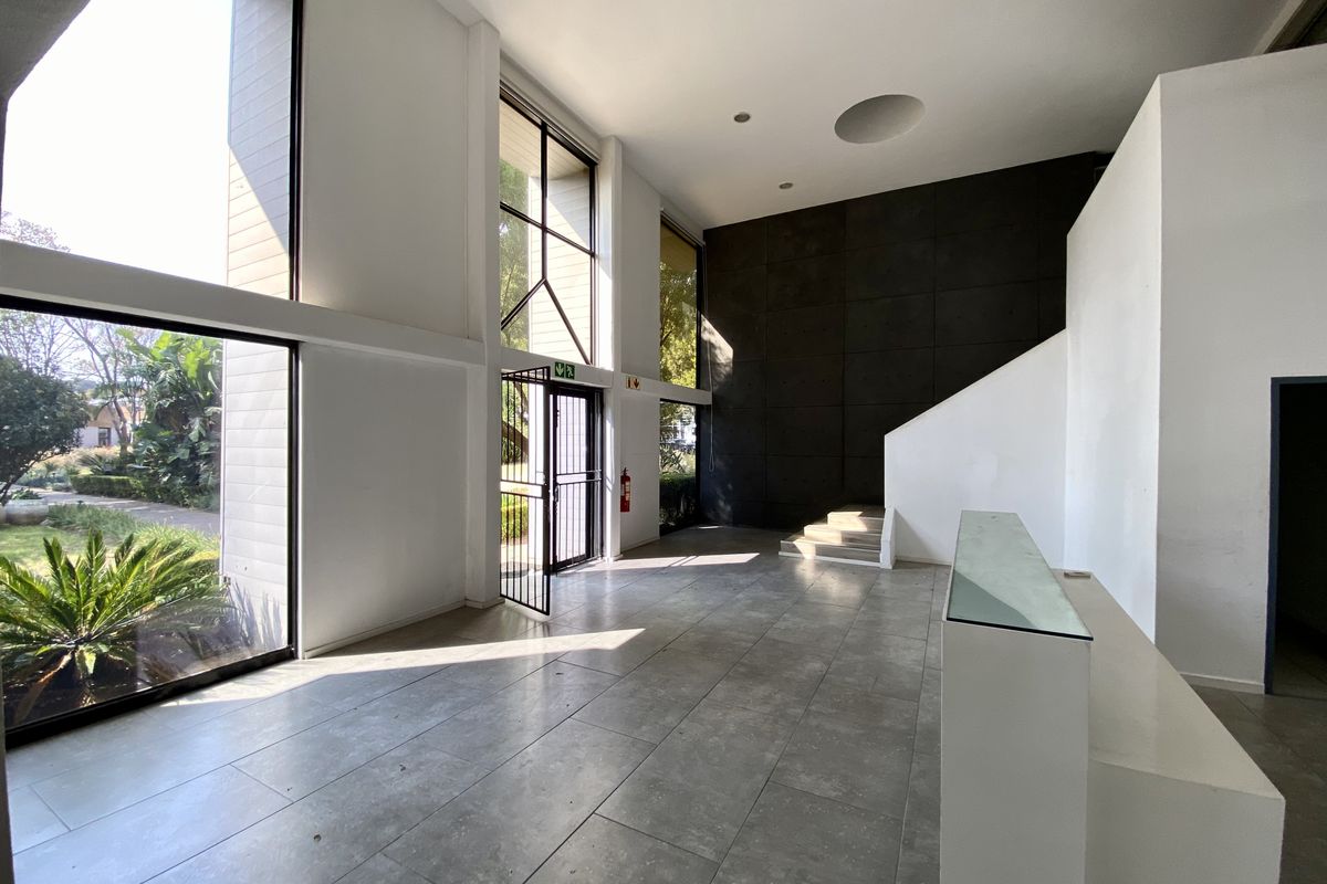 Spacious double-volume office entrance lobby featuring large windows, tiled flooring, and a built-in reception desk with modern architectural design.