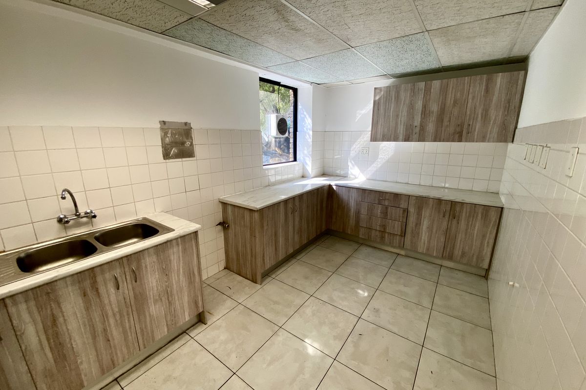 A functional office kitchenette featuring laminate cabinetry, double bowl stainless steel sink, tiled splashback, and ceramic floor tiles under a drop ceiling.