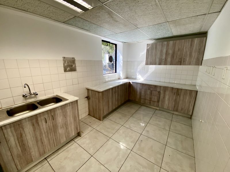 A functional office kitchenette featuring laminate cabinetry, double bowl stainless steel sink, tiled splashback, and ceramic floor tiles under a drop ceiling.