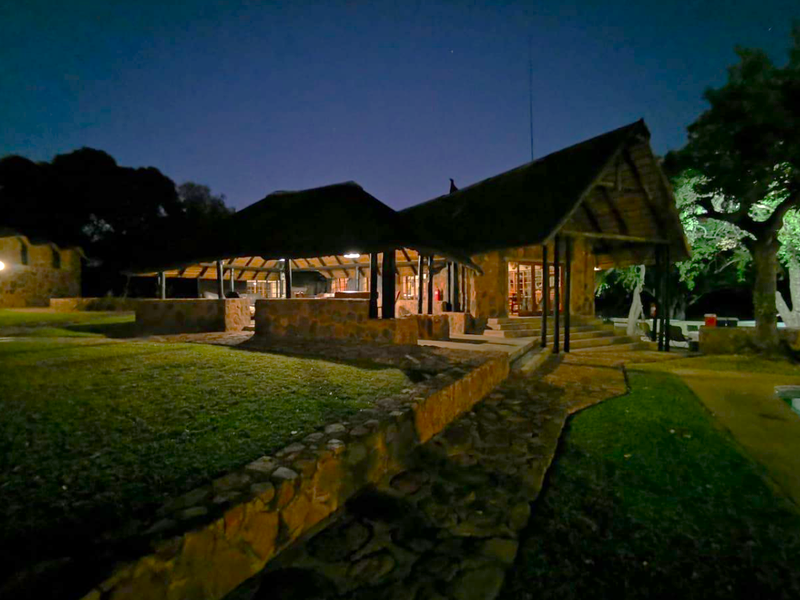 Night view of a rustic farm-style dwelling featuring a thatched roof, stone masonry construction, and an expansive covered patio area overlooking the garden.