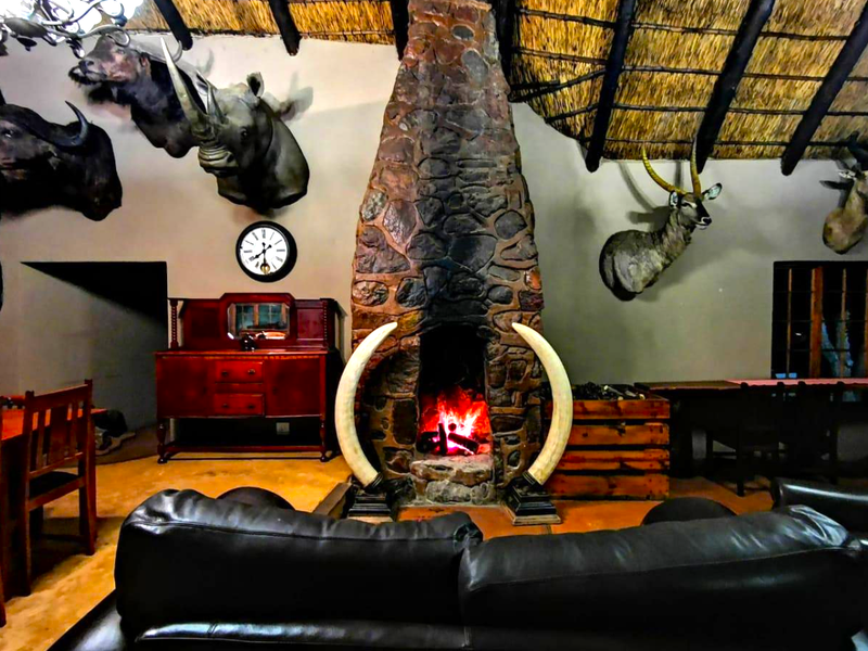 Spacious living area featuring a prominent stone fireplace, exposed timber beams, and a traditional thatched roof ceiling.