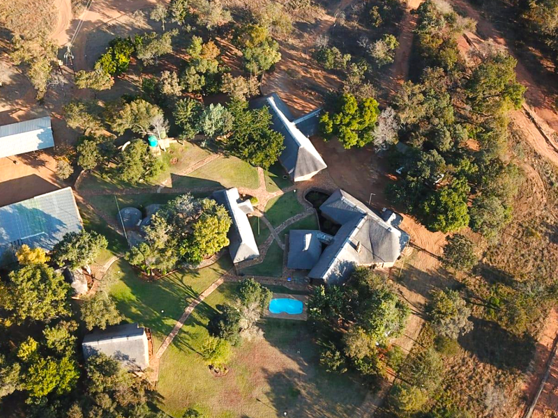 Aerial view of a farm property featuring multiple thatched-roof buildings, a swimming pool, and extensive landscaped grounds with mature trees and paved pathways.