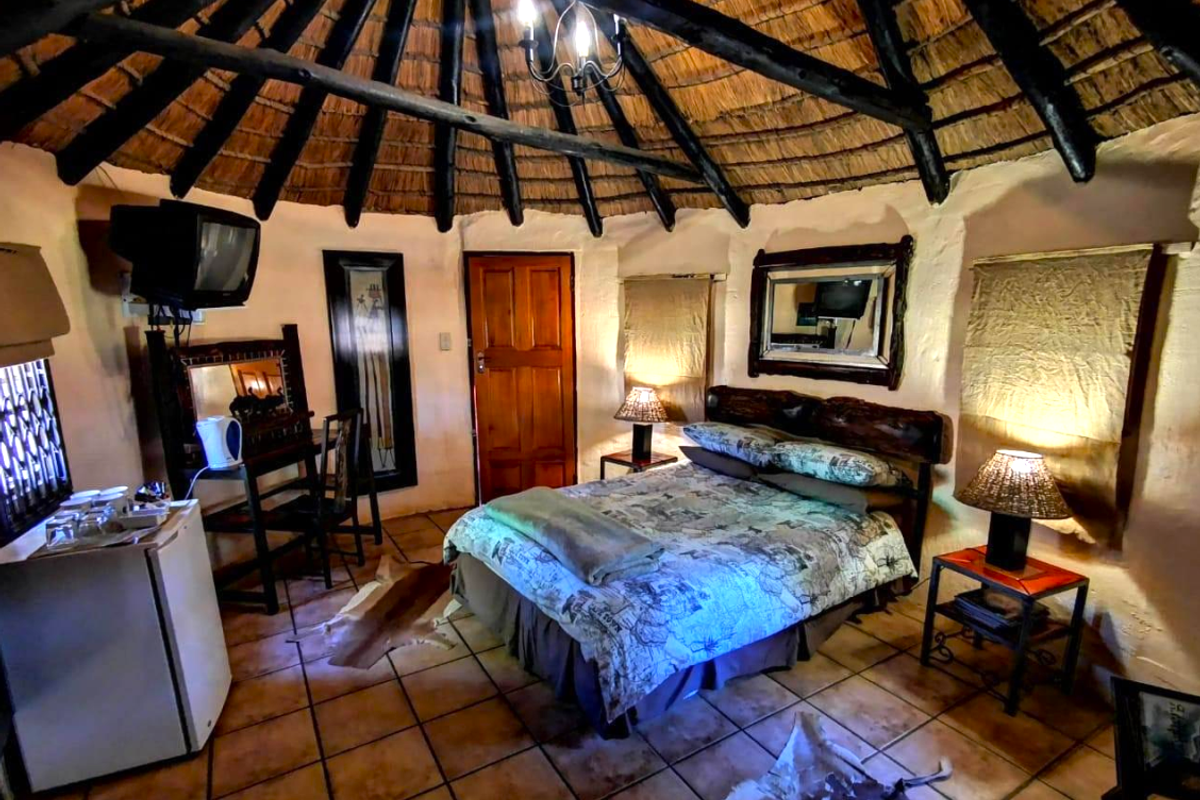 A rustic bedroom featuring a traditional thatched roof with exposed timber rafters, tiled flooring, and a warm, cozy atmosphere.