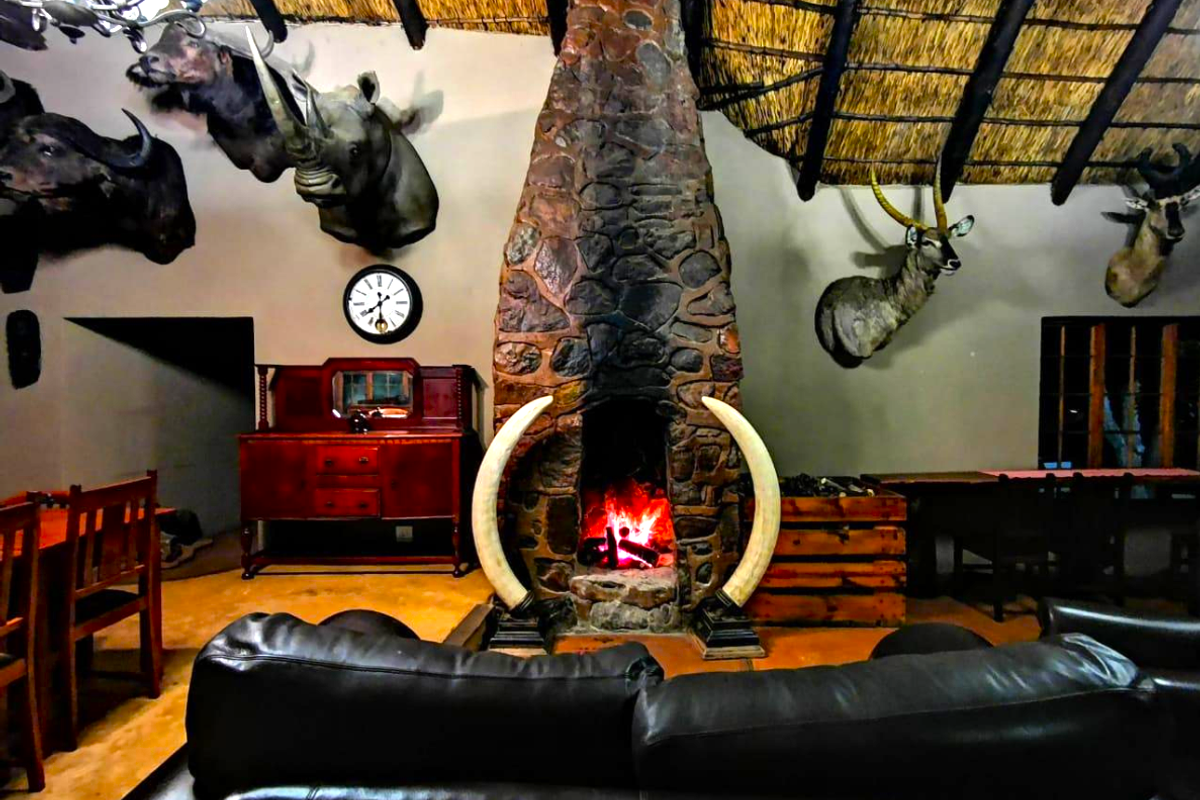 Spacious living area featuring a prominent stone fireplace, exposed timber beams, and a traditional thatched roof ceiling.