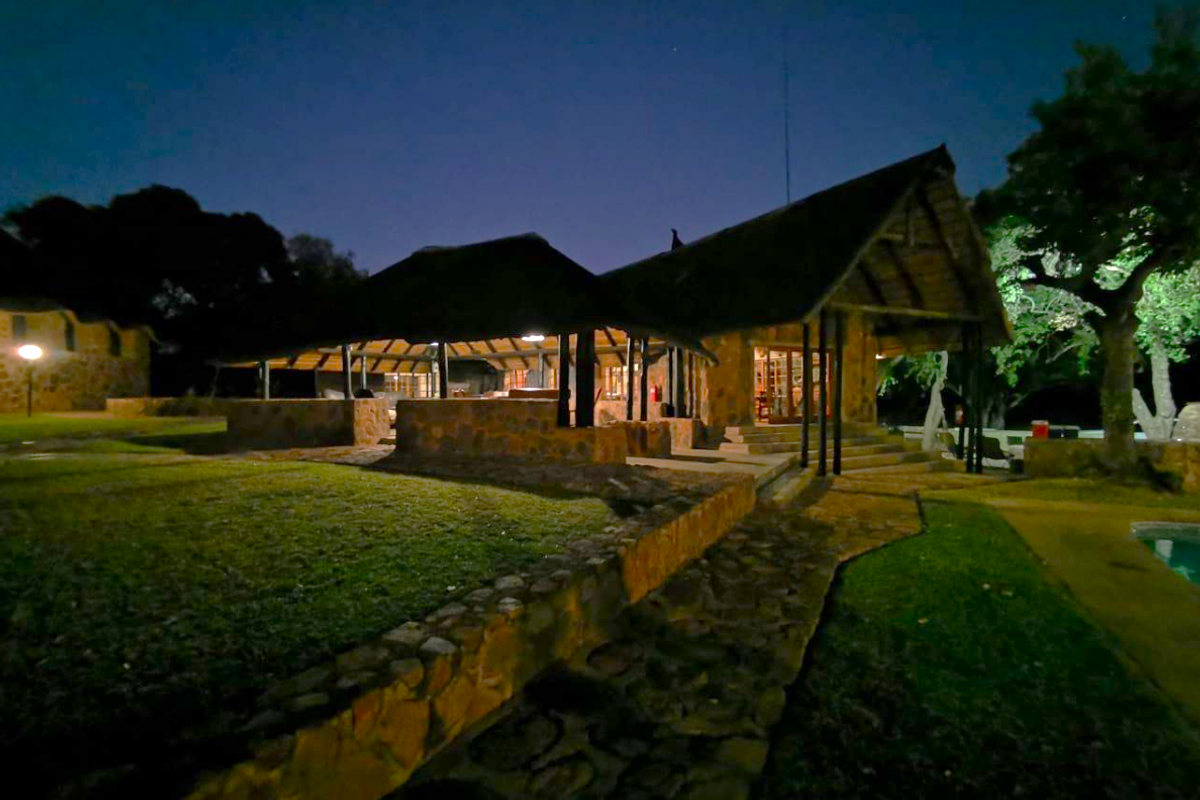 Night view of a rustic farm-style dwelling featuring a thatched roof, stone masonry construction, and an expansive covered patio area overlooking the garden.