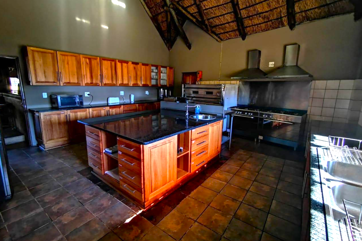 Spacious farm-style kitchen featuring extensive wooden cabinetry, granite countertops, a central island, and professional-grade cooking appliances under a high thatched roof.