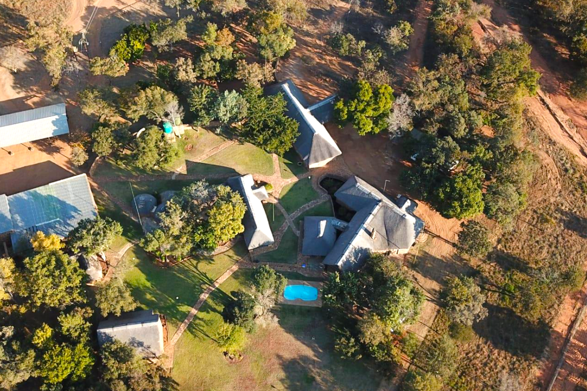 Aerial view of a farm property featuring multiple thatched-roof buildings, a swimming pool, and extensive landscaped grounds with mature trees and paved pathways.