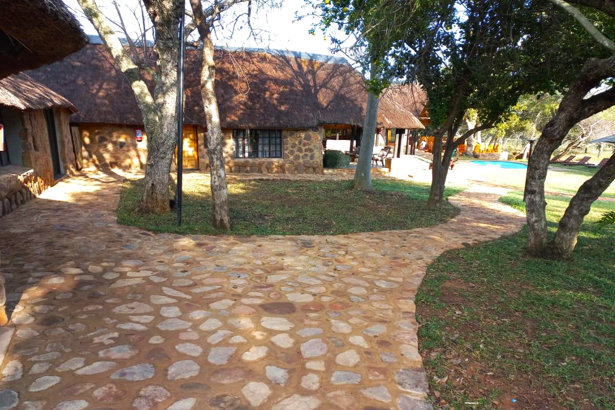 Rear view of a rustic farm-style dwelling featuring traditional thatched roofing, stone exterior walls, and a stone-paved courtyard leading to a swimming pool area.