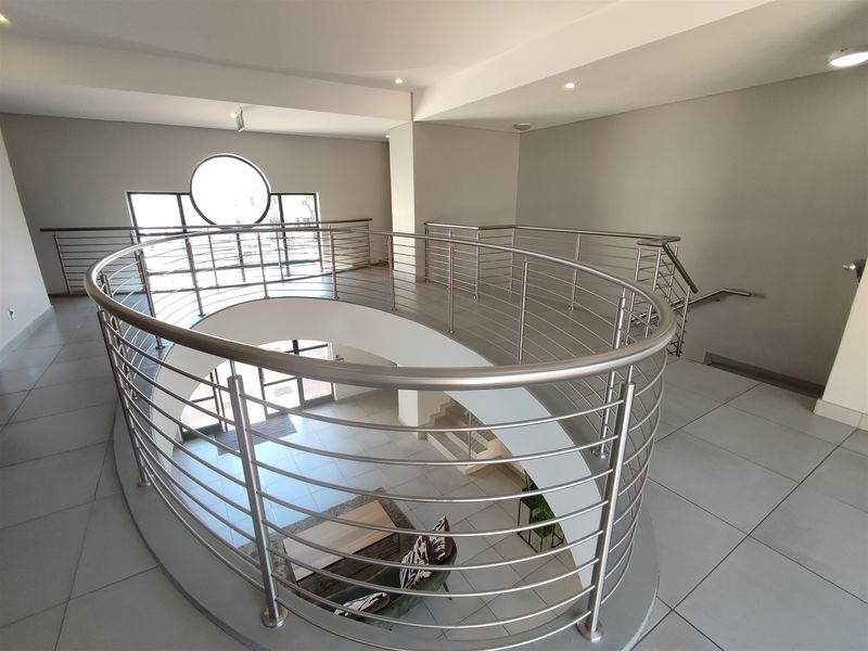 Spacious office building landing featuring a modern curved stainless steel balustrade, tiled flooring, and a distinctive circular window.