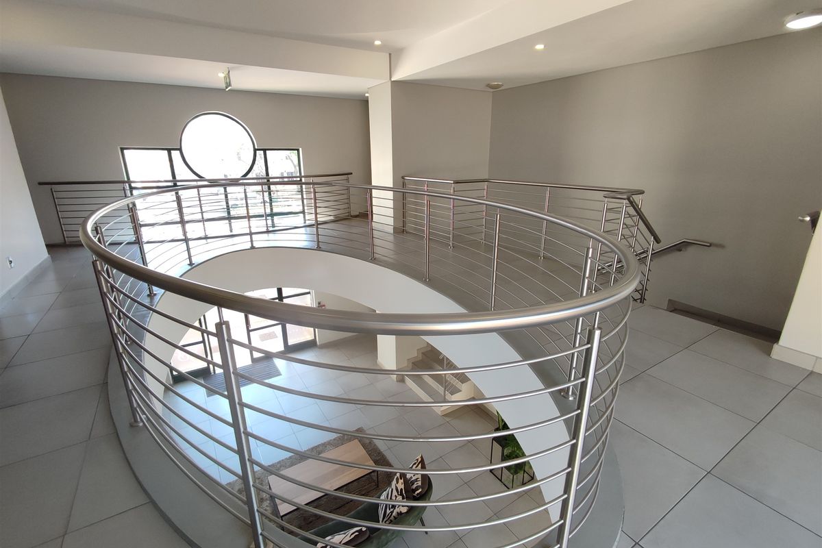 Spacious office building landing featuring a modern curved stainless steel balustrade, tiled flooring, and a distinctive circular window.