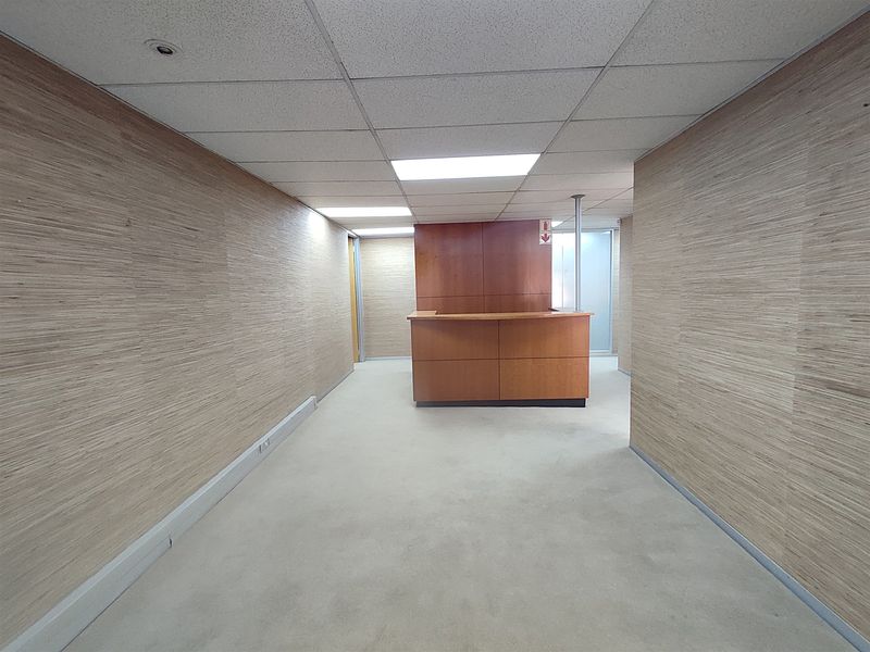An empty office space featuring wood veneer wall paneling, a built-in reception desk, and a suspended ceiling with recessed lighting.