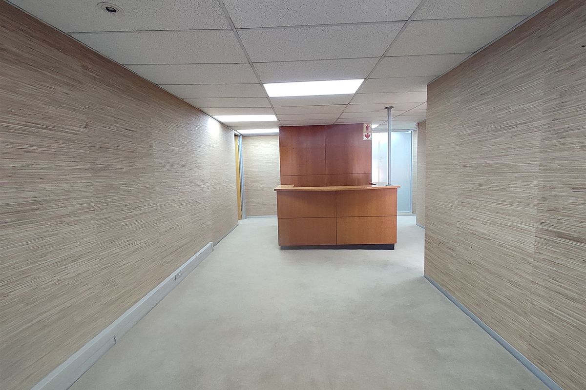 An empty office space featuring wood veneer wall paneling, a built-in reception desk, and a suspended ceiling with recessed lighting.