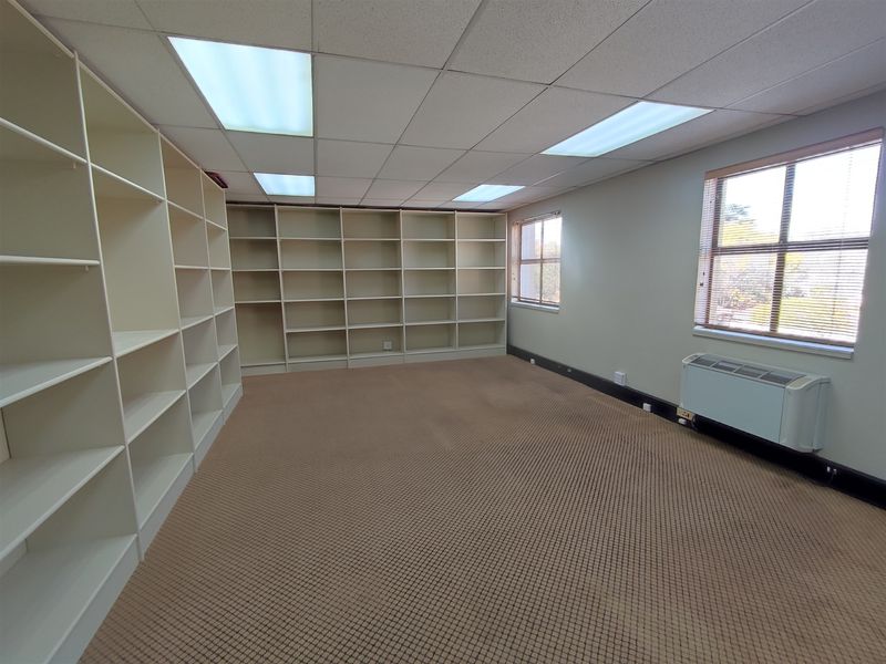 A vacant office space featuring built-in shelving units, suspended ceiling with recessed lighting, and an integrated HVAC unit.