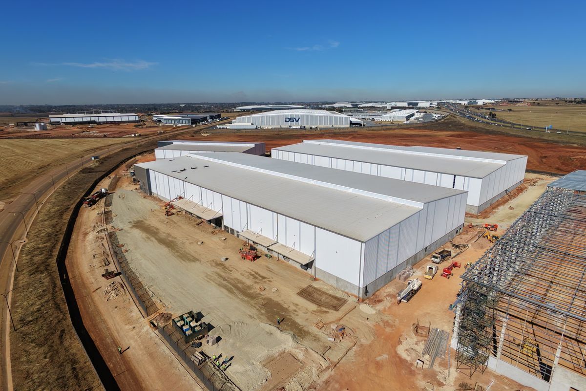 Aerial view of a large industrial warehouse facility under construction, featuring expansive metal roofing and steel frame structures on a developing site.