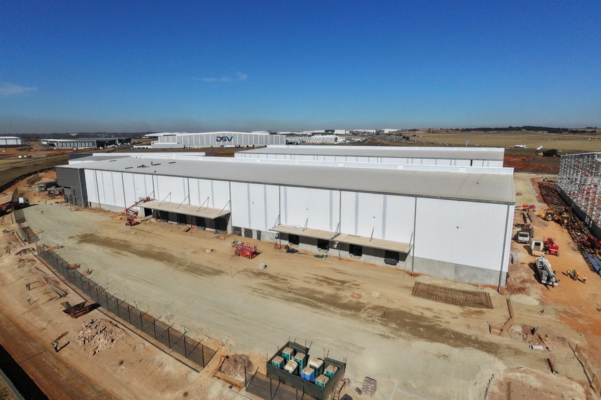 Aerial view of a large industrial warehouse facility under construction, featuring extensive metal cladding, loading bays, and surrounding site development.