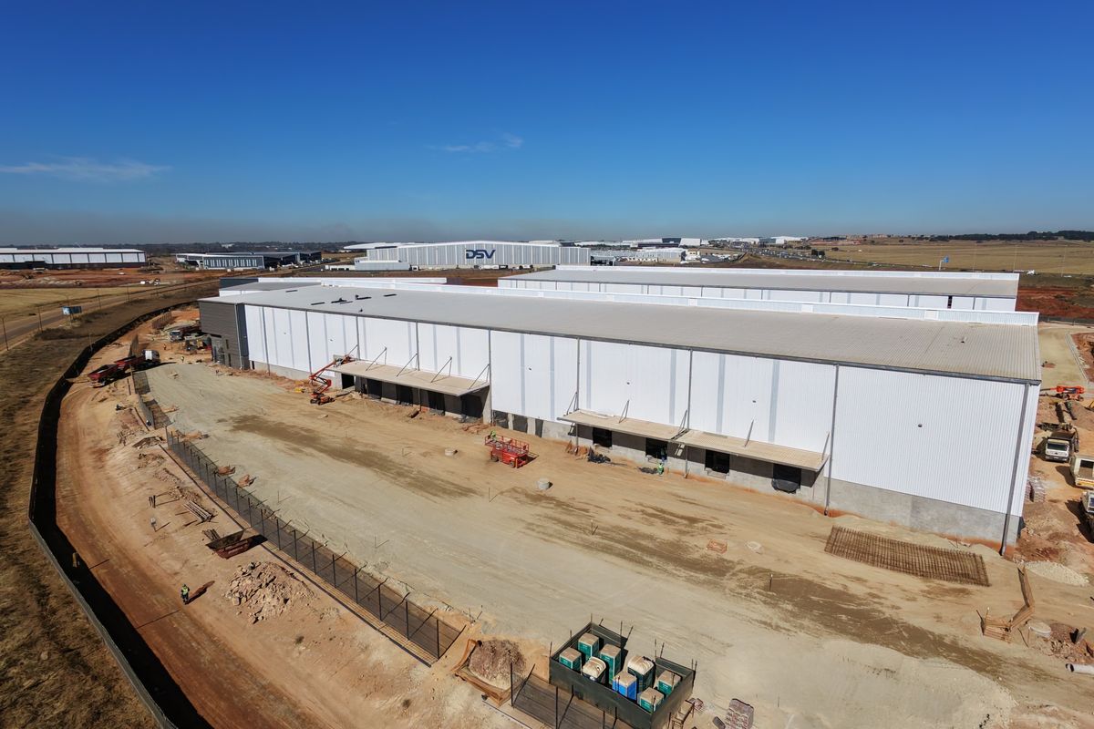 Aerial view of a large industrial warehouse facility under construction, featuring extensive metal cladding, loading bays, and surrounding site development.