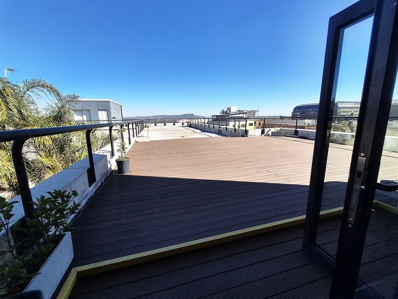A spacious rooftop balcony featuring composite decking, metal safety railings, and wide-opening glass doors with expansive city views.