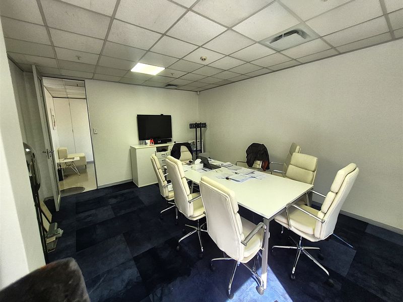 A functional office meeting room featuring a suspended ceiling, recessed lighting, and dark carpet tiles, providing a professional workspace environment.