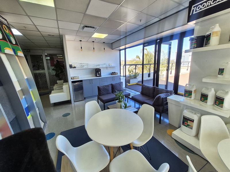A bright office break area featuring a built-in kitchenette, suspended ceiling, and direct access to an outdoor balcony through large glass sliding doors.