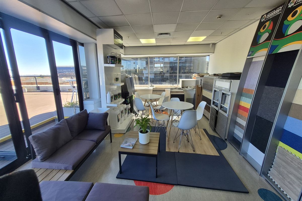 A bright office space featuring large windows, sliding glass doors leading to an outdoor area, suspended ceilings, and integrated product display shelving.