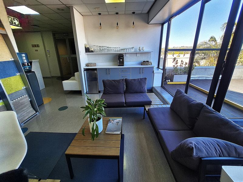 Modern office breakout area featuring a built-in kitchenette, ample natural light from floor-to-ceiling windows, and direct access to an outdoor balcony.