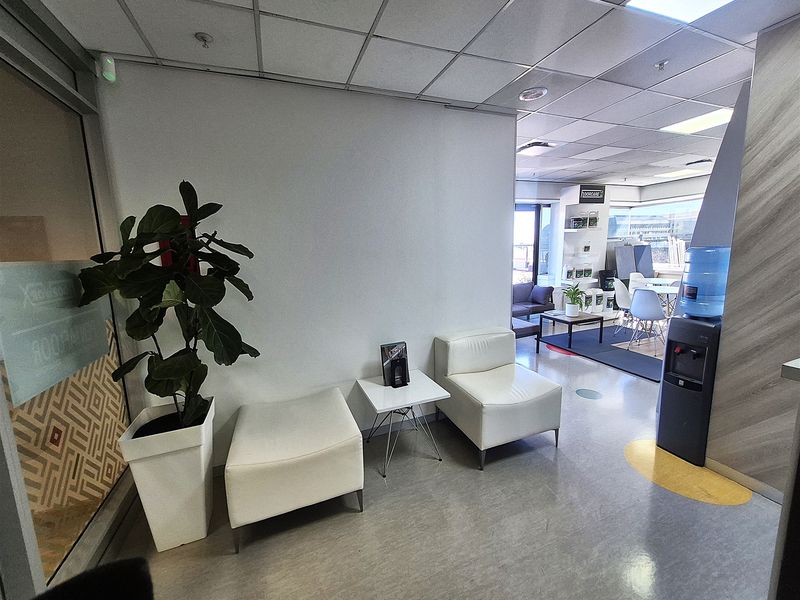 A functional office reception area featuring a suspended ceiling, vinyl flooring, and a glass partition, leading into an open-plan workspace.