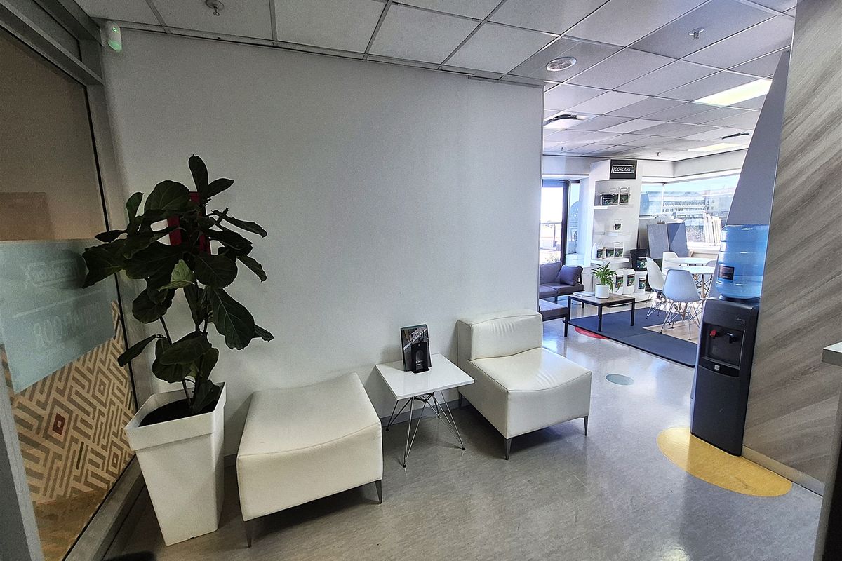 A functional office reception area featuring a suspended ceiling, vinyl flooring, and a glass partition, leading into an open-plan workspace.