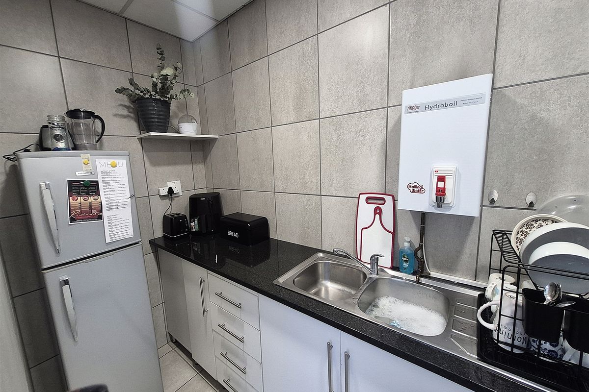 A functional office kitchenette featuring granite countertops, stainless steel sink, wall-mounted boiling water dispenser, and tiled finishes.