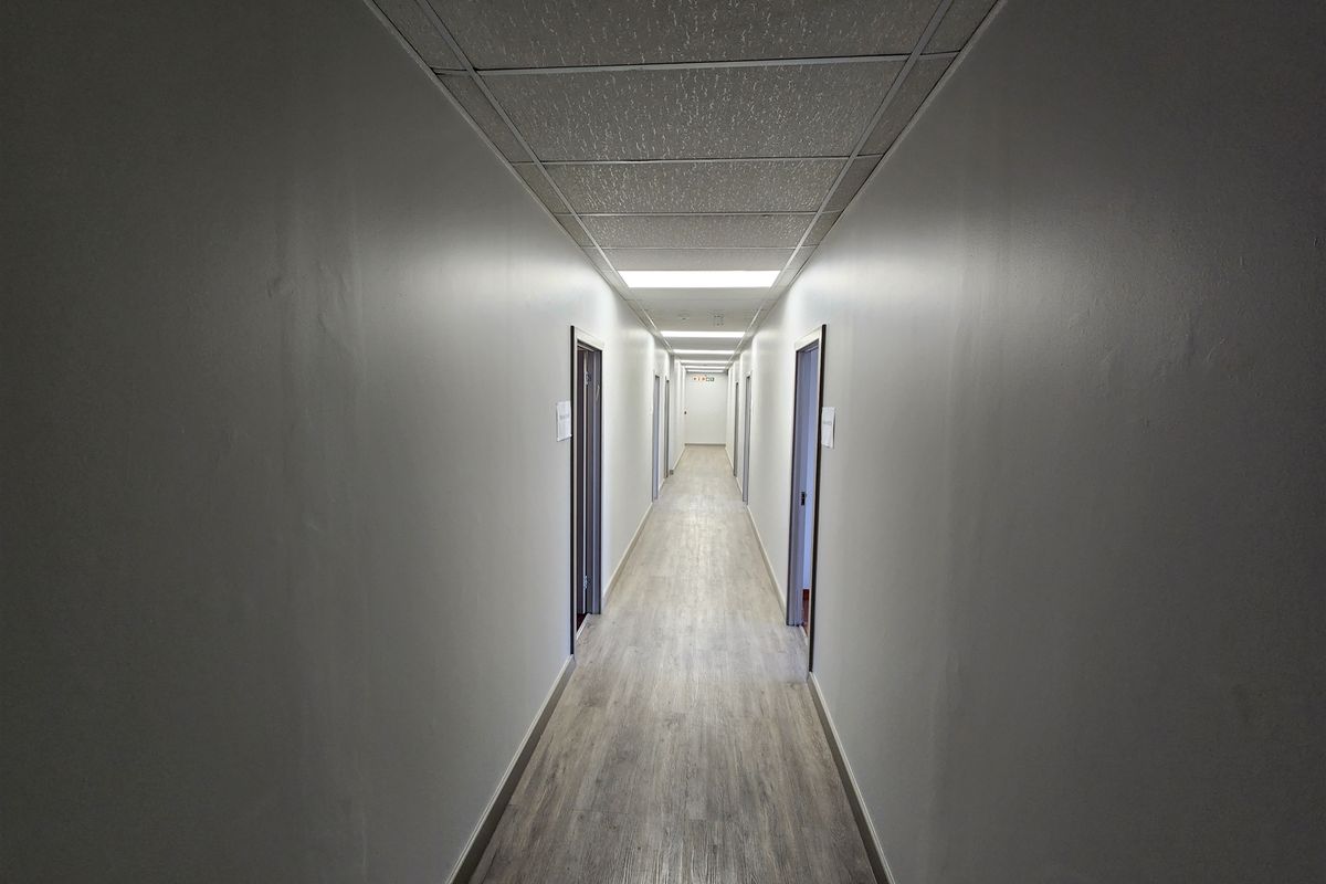 A clean, well-lit office hallway featuring modern laminate flooring, a suspended ceiling with recessed lighting, and multiple access doors.