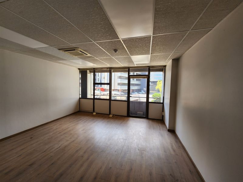 An empty office space featuring laminate flooring, a suspended ceiling with integrated lighting, and large windows providing natural light and urban views.
