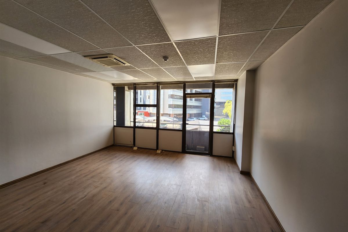 An empty office space featuring laminate flooring, a suspended ceiling with integrated lighting, and large windows providing natural light and urban views.