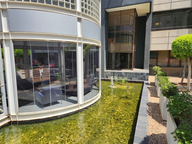 Modern office exterior featuring a curved glass block facade, floor-to-ceiling glazing, and a decorative water feature with stone detailing.