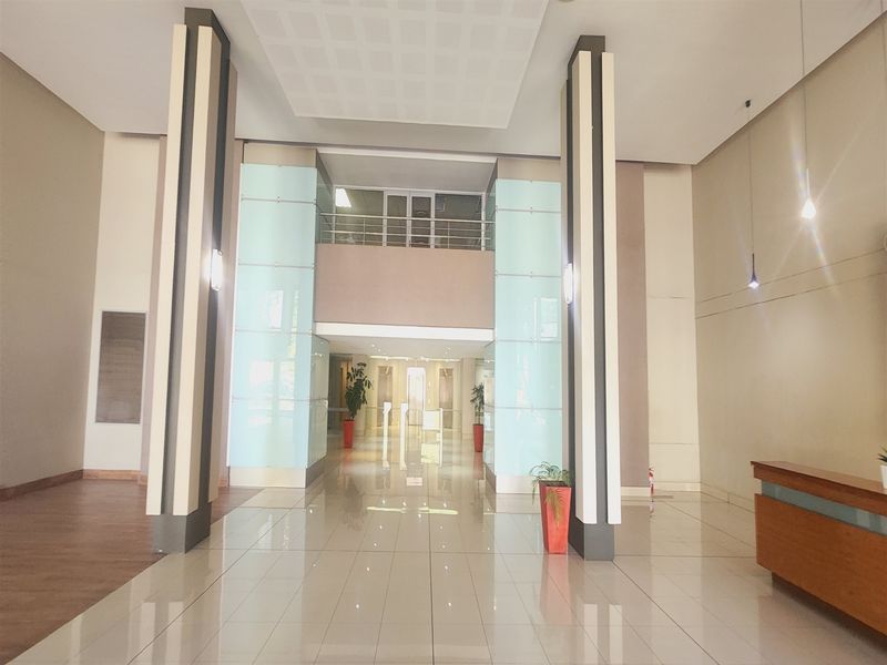 Spacious office building entrance lobby featuring high ceilings, tiled flooring, glass architectural accents, and a built-in reception desk.