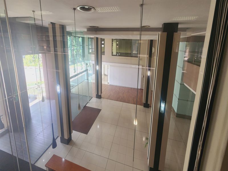 Spacious double-volume office entrance lobby featuring modern glass facade, tiled flooring, and architectural pillars, providing a bright and professional reception area.