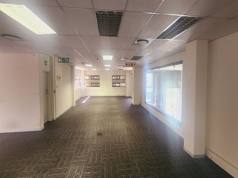 An empty, open-plan office space featuring suspended ceilings, recessed lighting, carpet tiles, and a large glass partition wall.