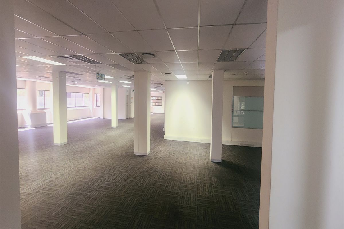 Spacious open-plan office area featuring neutral carpet tiles, structural columns, and a suspended ceiling with recessed lighting, offering a versatile workspace.