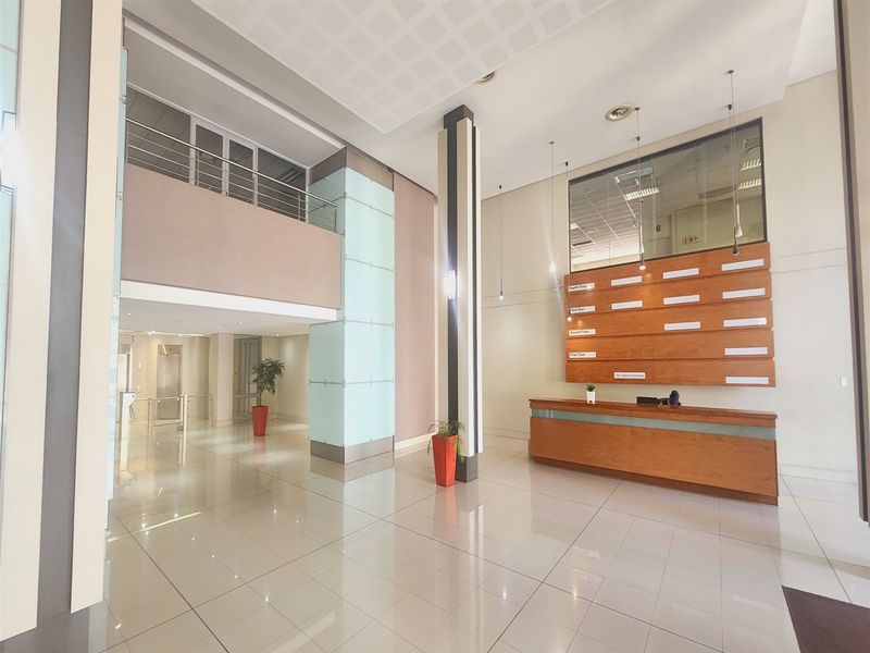 Spacious office building entrance lobby featuring a built-in reception desk, directory board, high ceilings, and polished tiled flooring with a mezzanine level.