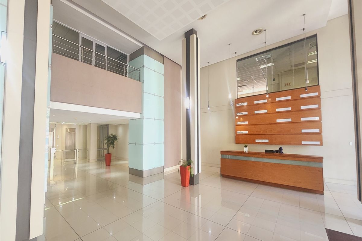 Spacious office building entrance lobby featuring a built-in reception desk, directory board, high ceilings, and polished tiled flooring with a mezzanine level.