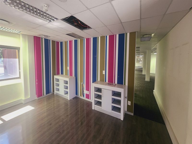 Empty office space featuring laminate flooring, suspended ceiling with lighting, and vibrant striped wallpaper, requiring minor ceiling repairs.