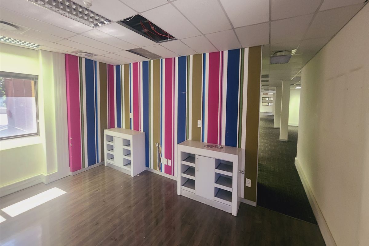 Empty office space featuring laminate flooring, suspended ceiling with lighting, and vibrant striped wallpaper, requiring minor ceiling repairs.