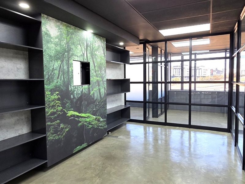 Modern office space featuring polished concrete floors, extensive glass partitioning, and built-in shelving with a decorative forest-themed feature wall.