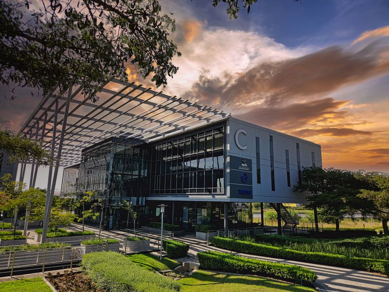 Modern office building exterior featuring a glass facade, extensive steel pergola structure, and well-maintained landscaped grounds at sunset.