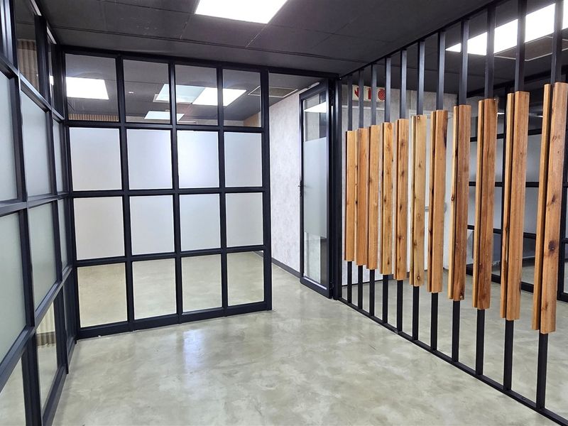 Modern office space featuring sleek black metal and frosted glass partitions, polished concrete floors, and a contemporary timber slat feature wall.