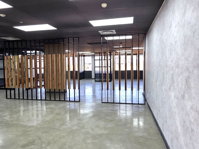 Modern open-plan office space featuring polished concrete floors, contemporary timber slat partitions, and a sleek black suspended ceiling with recessed lighting.